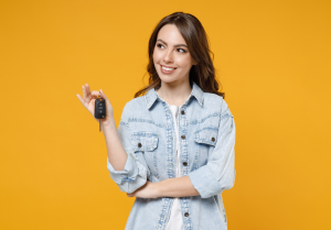 A person holding a set of car keys in front of a yellow background near Carmel, IN