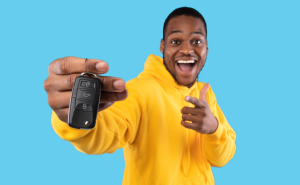 A person holding up and pointing to the keys to their new car on a blue nabkground near Carmel, Indiana